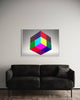 A Black Couch with one black and white textured pillow sits on the wood panelled floor directly in front of a white wall. Above the couch is a beautiful 60 x 40 inch photograph of a large colourful cube with sections in cyan, yellow, magenta, green, red, purple, brown and black against a grey vignette background and framed with this ½ inch white wood.